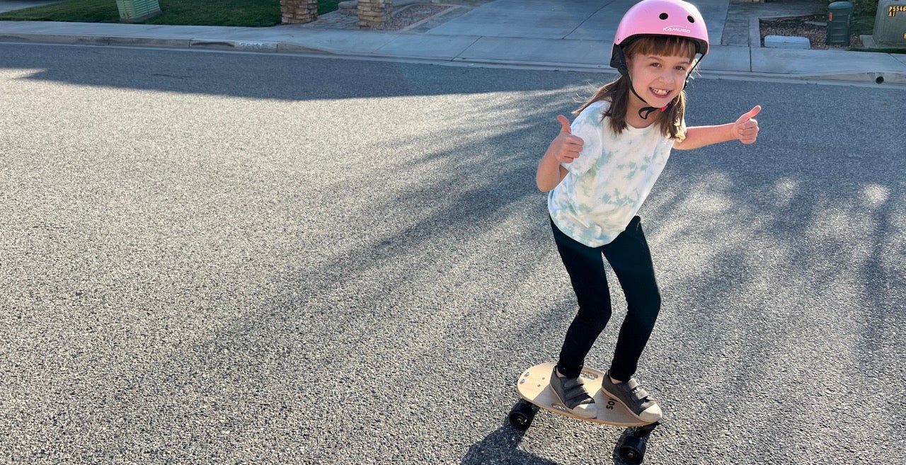 A girl in a helmet riding an Elos board and giving a thumbs-up