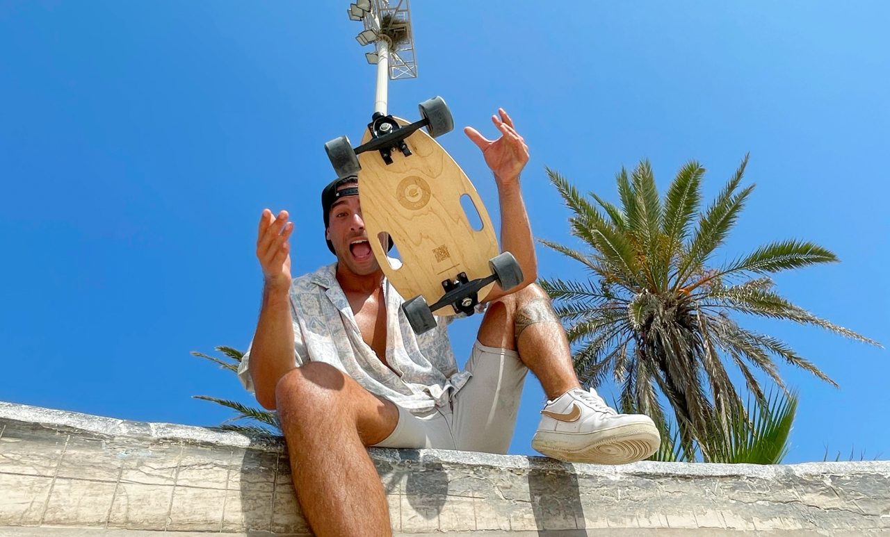 A man tossing an Elos board into the air under palm trees
